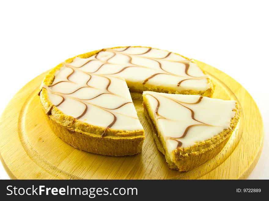 Delicious looking iced bakewell tart on a wooden platter with a plain background