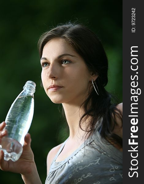 Beautiful young woman in the park. Drinks water.