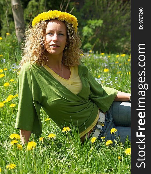 Curly girl with dandelion chain on head sitting on meadow in blossom