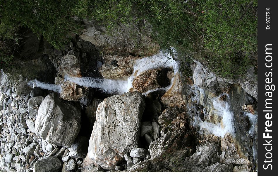 Brook falling in stages between rocks and pebbles in valley. Brook falling in stages between rocks and pebbles in valley