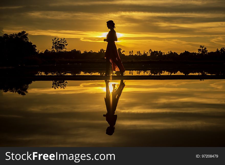 Silhouette of Man Standing on Lake at Sunset