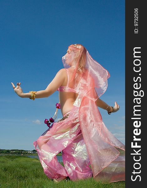 A woman in pink asian dress dancing on the grass and a blue sky. A woman in pink asian dress dancing on the grass and a blue sky