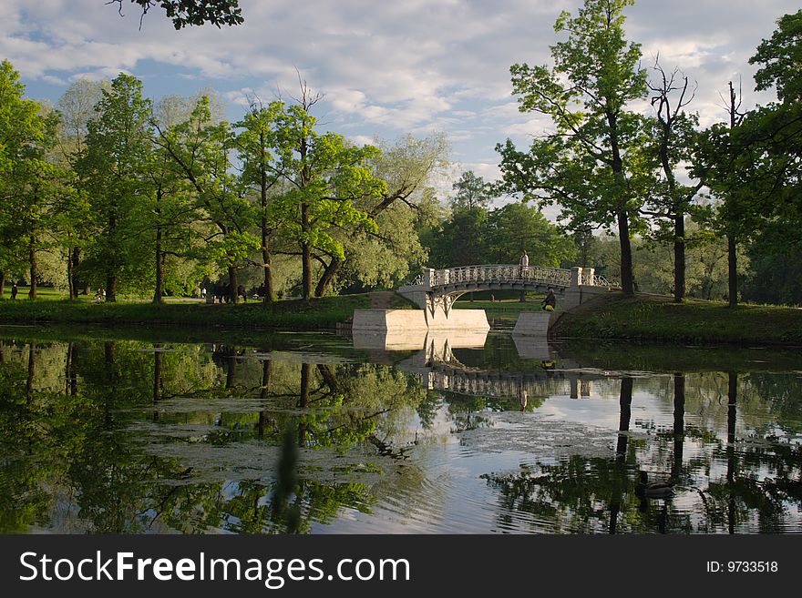 Old pedestrian bridge in a town park with reflection in a pond
