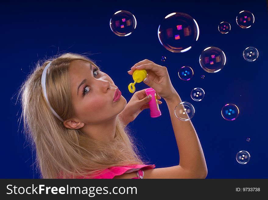 Young beautiful blond inflate soap bubbles on a blue background
