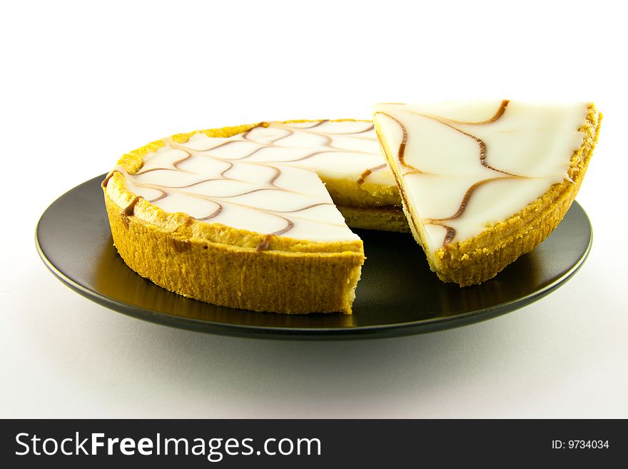 Delicious looking iced bakewell tart on a black plate with a plain background