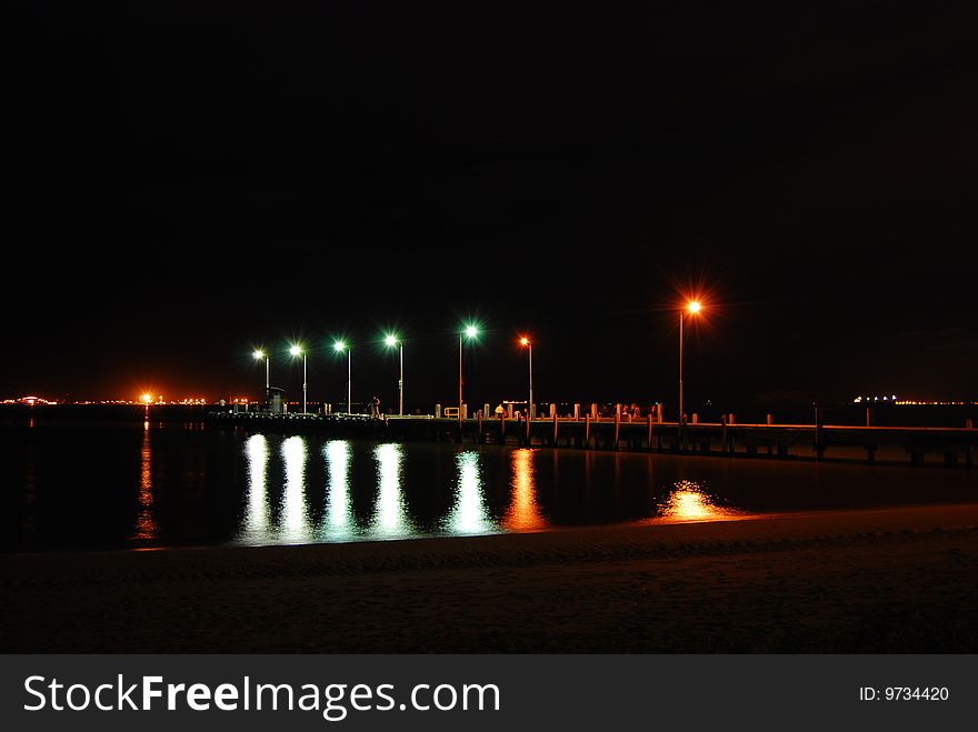 Rockingham jetty at night, waters of the ocean reflecting the green and red lights on the jetty. Fishermen come there every night to catch fish seeking shelter under the jetty.