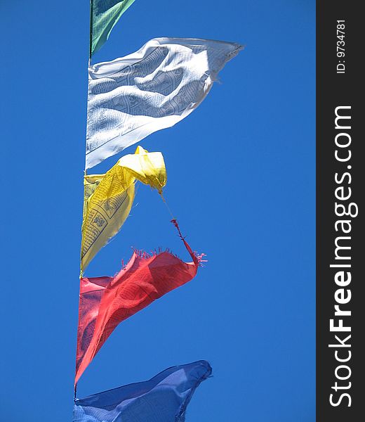 Colourful prayer flags against a blue sky, red and yellow entangled