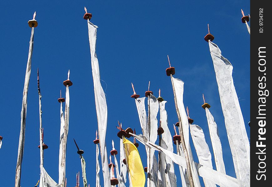 Prayer flag poles with printed flags cob=ntaining religious mantra, against a blue sky. Prayer flag poles with printed flags cob=ntaining religious mantra, against a blue sky