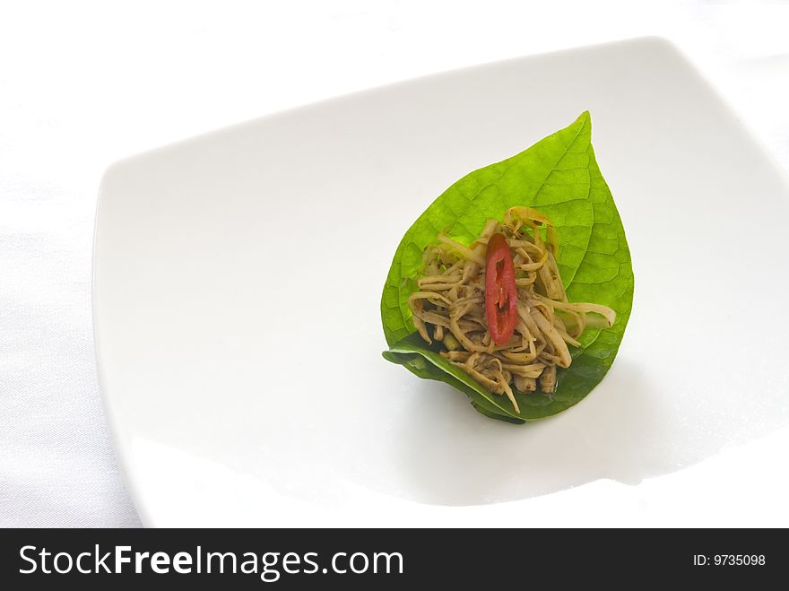 Spicy bamboo salad topped with a sliced red pepper, presented on a betel leaf and served on a white ceramic plate. Thai cuisine. ADOBE RGB (1998) color profile. Spicy bamboo salad topped with a sliced red pepper, presented on a betel leaf and served on a white ceramic plate. Thai cuisine. ADOBE RGB (1998) color profile