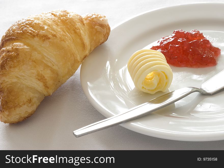 An image of a freshly baked croissant served on white ceramic plate with a portion of butter and jam. ADOBE RGB (1998) color profile. An image of a freshly baked croissant served on white ceramic plate with a portion of butter and jam. ADOBE RGB (1998) color profile.
