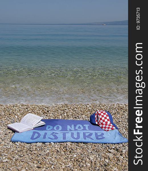Towel do not disturb with book and cap at beach near the Adriatic sea - Croatia (Dalmatia). Towel do not disturb with book and cap at beach near the Adriatic sea - Croatia (Dalmatia)