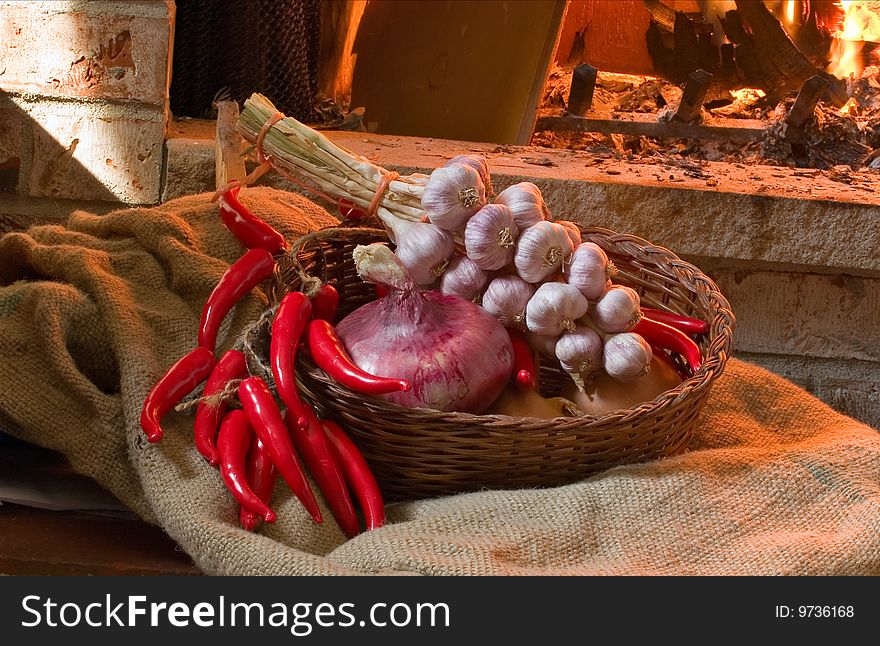 Garlic, onion and chili peppers in a wicker basket, lit by the fire in the fireplace. Garlic, onion and chili peppers in a wicker basket, lit by the fire in the fireplace