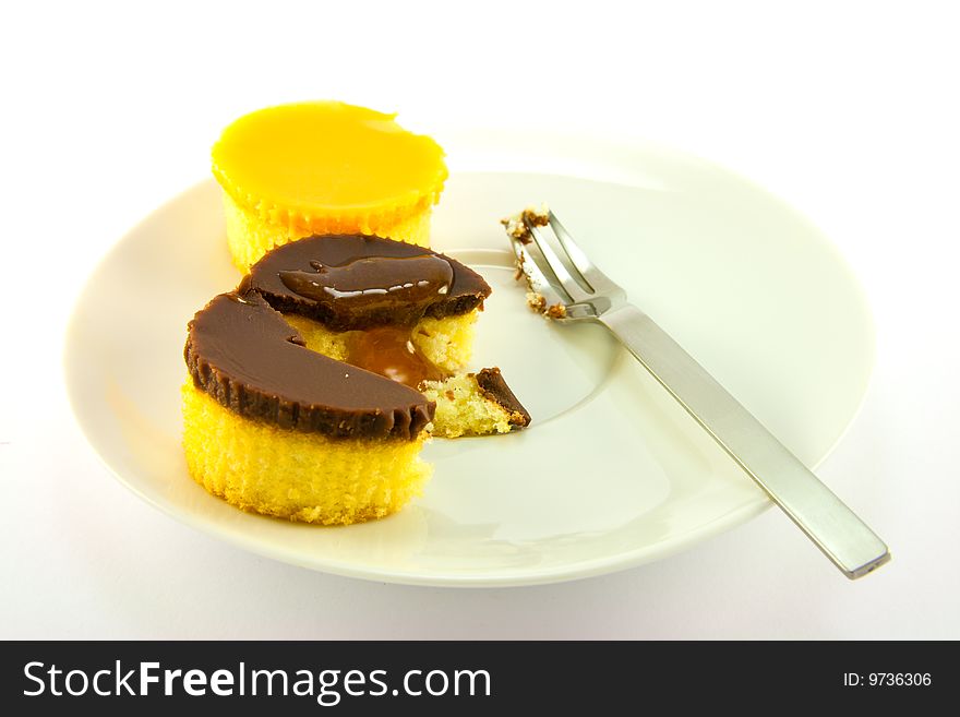 Two delicious looking cup cakes with a treacle drizzle resting on a white plate with a fork on a plain background. Two delicious looking cup cakes with a treacle drizzle resting on a white plate with a fork on a plain background