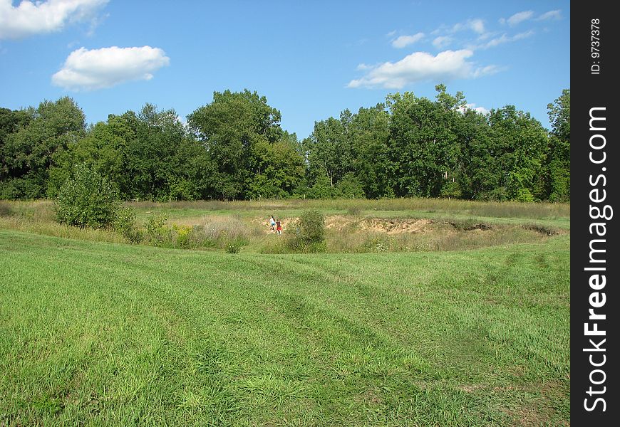 Children playing in the far distance in a large ditch, near a forest, in a meadow. Children playing in the far distance in a large ditch, near a forest, in a meadow.