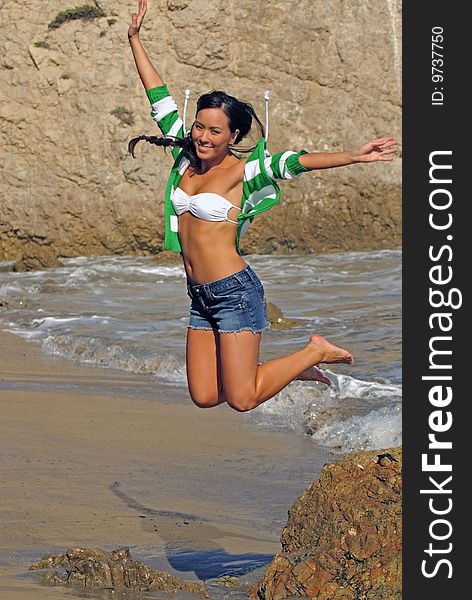 Beautiful hawaiian woman jumping off rock on beach