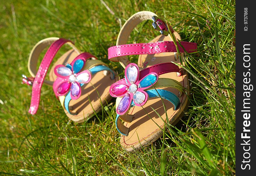 A little girl's pair of flowery colorful sandals lay on the grass. A little girl's pair of flowery colorful sandals lay on the grass