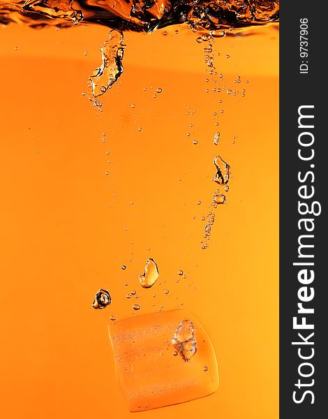 Ice with bubbles splashing underwater against orange background. Ice with bubbles splashing underwater against orange background