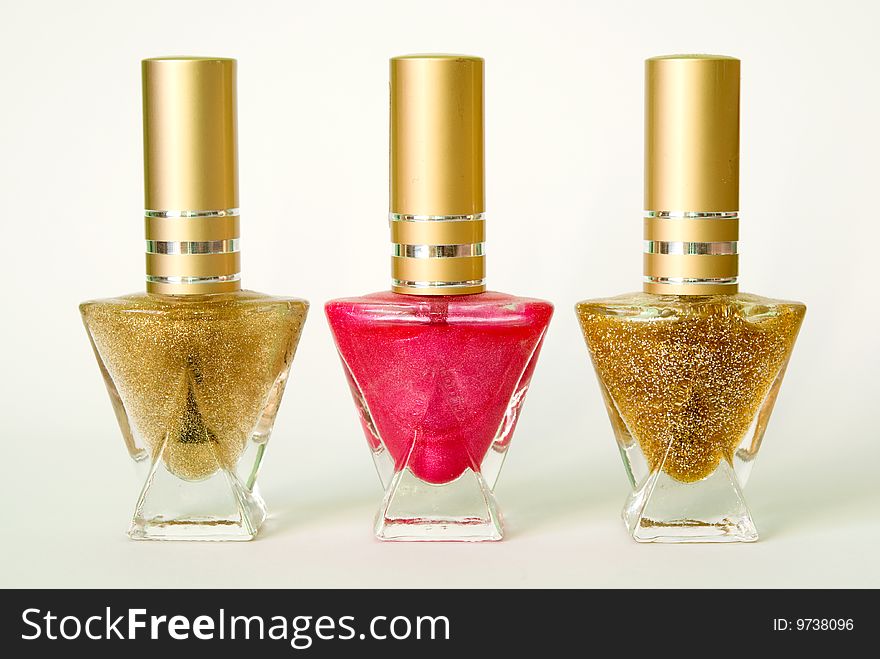 Thre bottles with nail varnish: one pink and two golden colours. Thre bottles with nail varnish: one pink and two golden colours