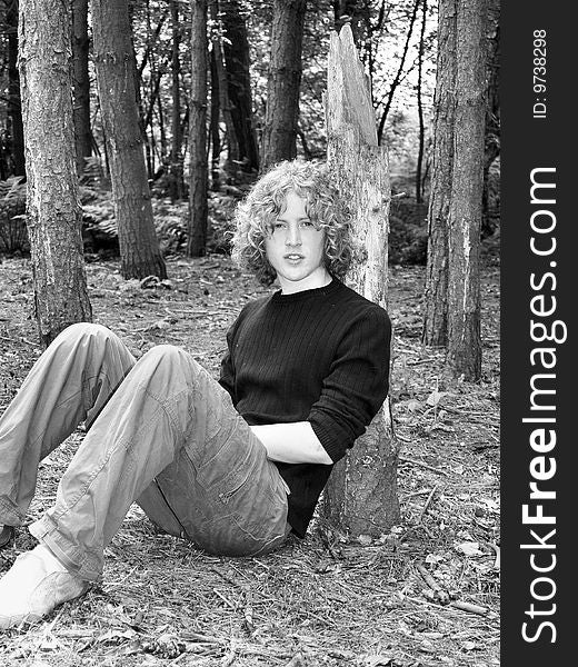 A black and white image of a teen sitting beside a tree in the woods. A black and white image of a teen sitting beside a tree in the woods