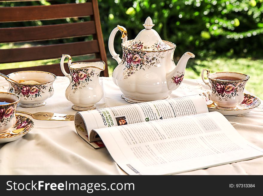 White and Pink Floral Ceramic Tea Set on White Textile Covered Table Beside White and Black Printed Book