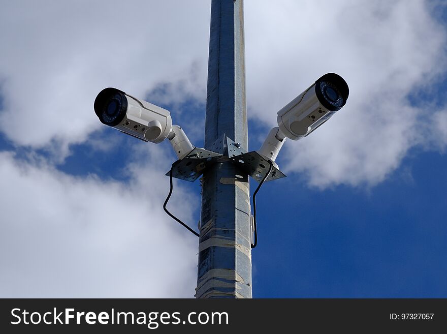 Two surveillance cameras on the same support on the street under the sky. Two surveillance cameras on the same support on the street under the sky