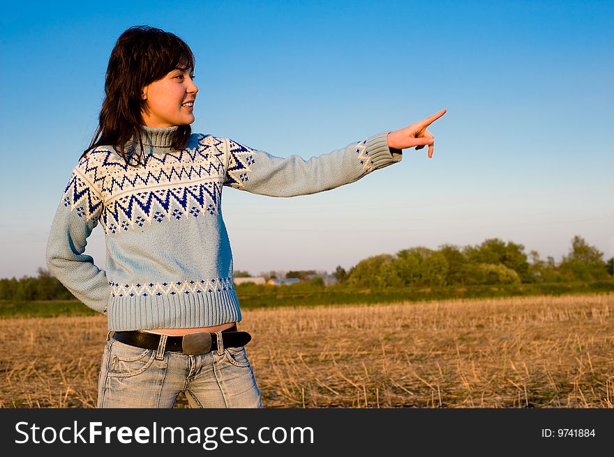 Smiling girl showing with finger. Outdoors with a field in the background