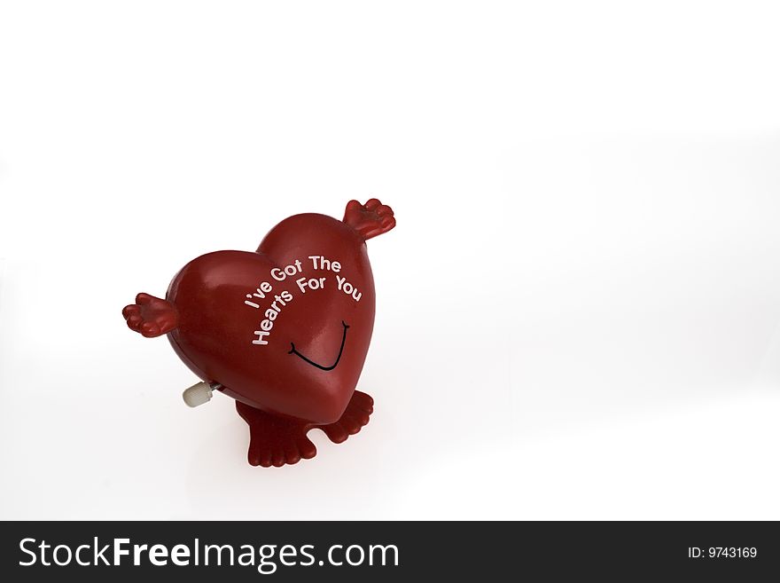 Red wind-up heart-shaped toy with arms open wide and standing on two feet, isolated against white background with ample copy space to the right and above. Red wind-up heart-shaped toy with arms open wide and standing on two feet, isolated against white background with ample copy space to the right and above