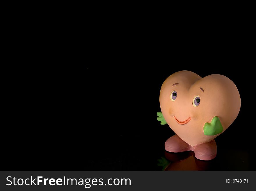 Cute heart-shaped doll showing the thumbs-up sign, isolated against black background with copy space on the left and above. Cute heart-shaped doll showing the thumbs-up sign, isolated against black background with copy space on the left and above