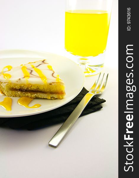 Delicious looking iced bakewell tart on a black plate with a treacle drizzle and a fork on a plain background