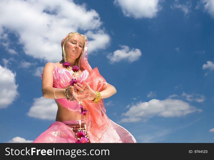 A woman in pink asian dress dancing and a blue sky. A woman in pink asian dress dancing and a blue sky