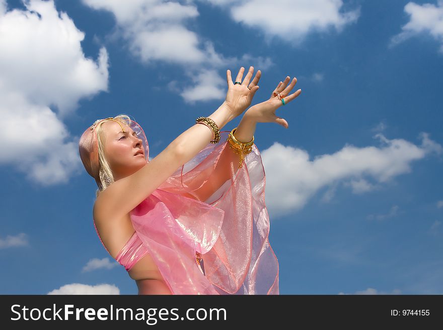 A woman in pink asian dress danccing and a blue sky