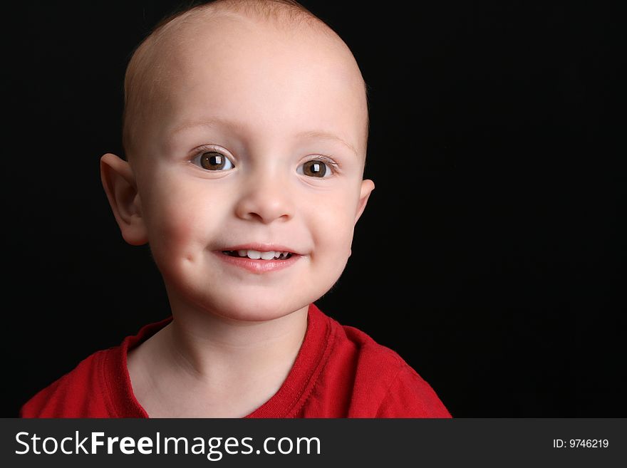Blonde toddler against a black background with a big smile