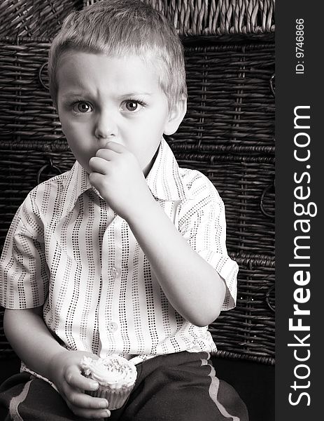 Serious toddler eating a cup cake, sitting against drawers