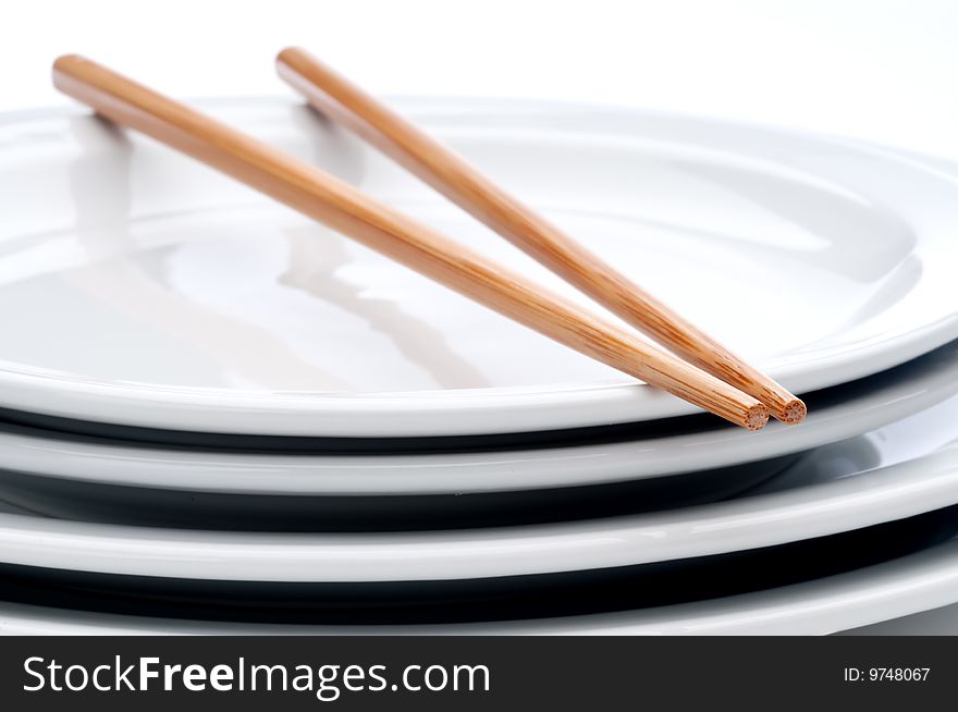 A horizontal close up of a pair of chopsticks on a stack of white plates
