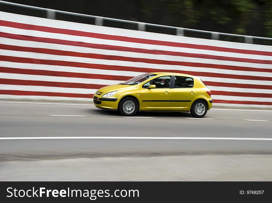 A small yellow car with some motion blur being driven next to a red and wall. ADOBE RGB color profile. A small yellow car with some motion blur being driven next to a red and wall. ADOBE RGB color profile