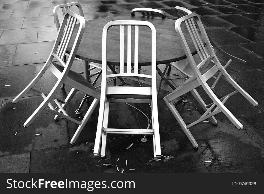 Sidewalk cafe chairs leaning against an empty table on a rainy day. Monochrome makes it moody. Sidewalk cafe chairs leaning against an empty table on a rainy day. Monochrome makes it moody.