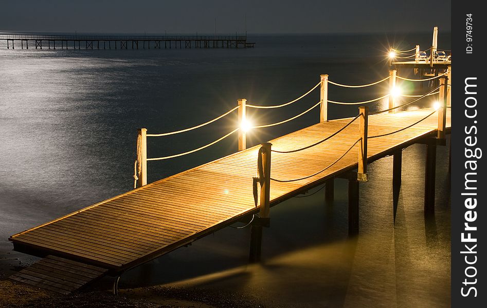 Night pier with lights, moon reflection on the water