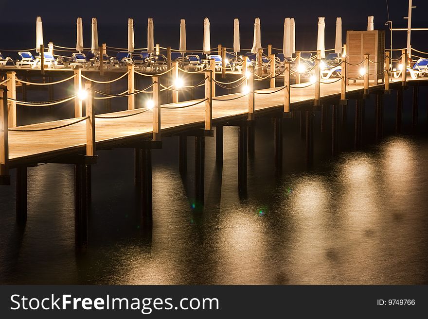 Night pier with lights, moon reflection on the water
