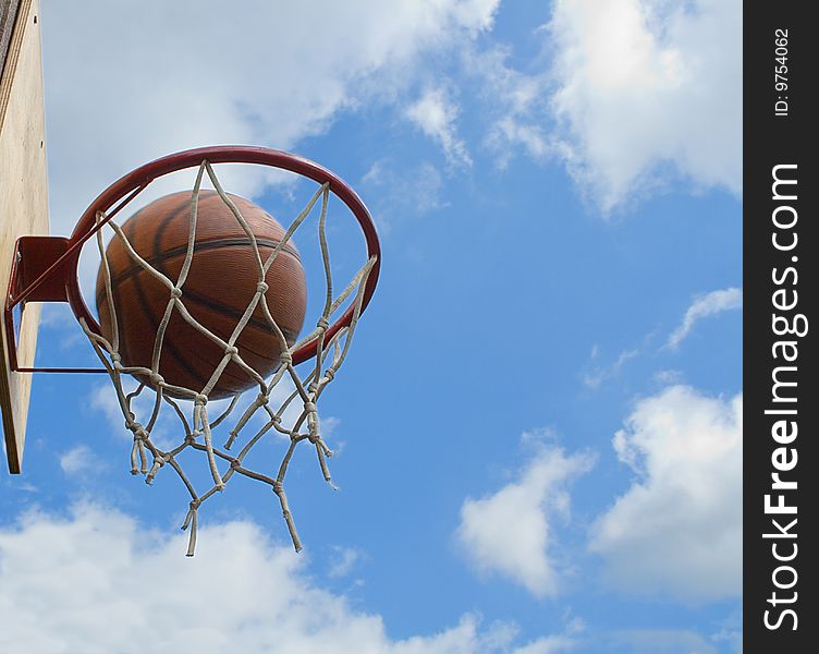 Action shot of basketball going through basketball hoop and net on clouds and blue sky backgrounds. Action shot of basketball going through basketball hoop and net on clouds and blue sky backgrounds