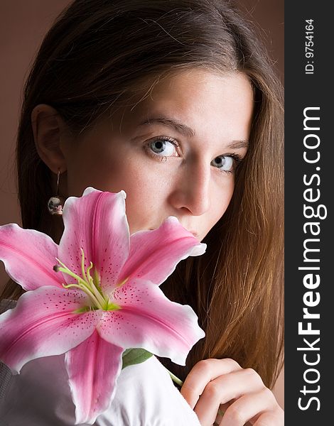 A pretty young woman with long brown hair posing with a pink lily in her hand. A pretty young woman with long brown hair posing with a pink lily in her hand