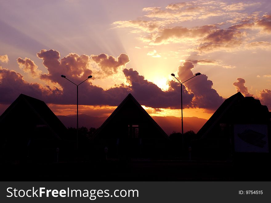 Sun burning through clouds and silhouettes of houses. Sun burning through clouds and silhouettes of houses
