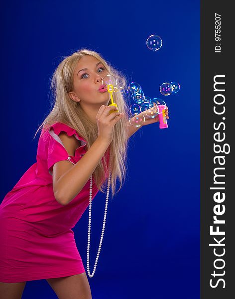 Young beautiful blond inflate soap bubbles on a blue background