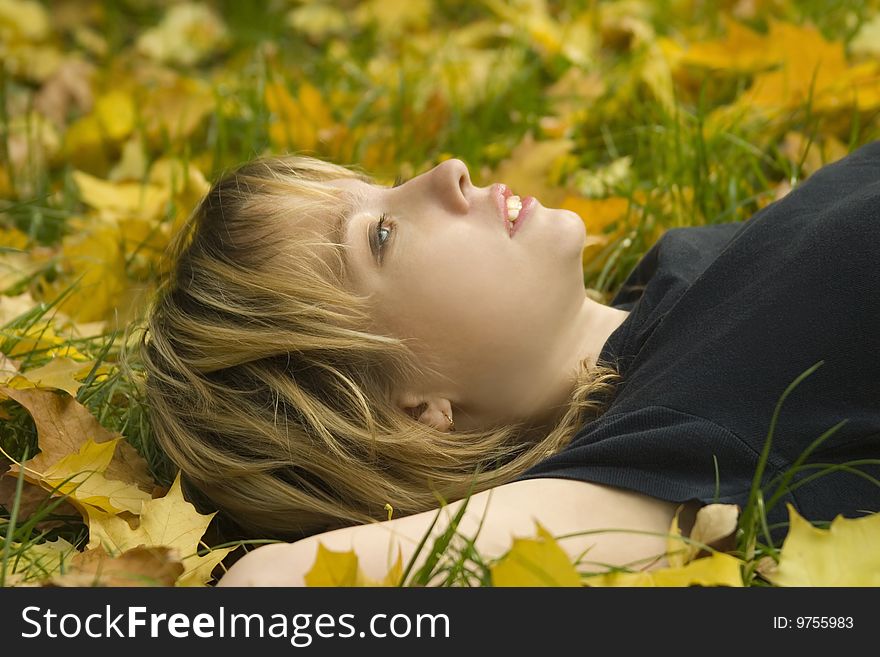 Young girl lying on the grass in the autumn leaves, and look up