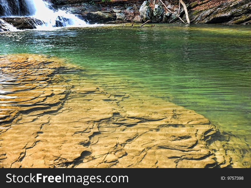 A deep green pool of water at the base of a waterfall.  Rocks under the water in the foreground. A deep green pool of water at the base of a waterfall.  Rocks under the water in the foreground.