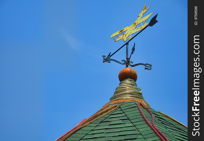 A wind compass with a biplane pointing Northeast sits atop a gazebo against a rich blue sky.