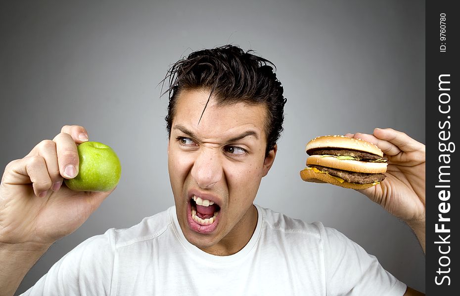 Man holds apple and burger while looking agitated. Man holds apple and burger while looking agitated