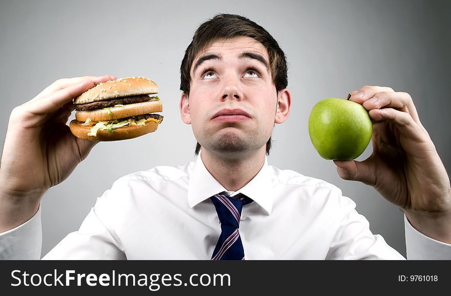 Yooung business man holds apple and burger. Yooung business man holds apple and burger