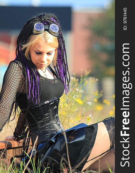Gothic woman with blond long hair in black corset and latex mini skirt sitting on the ground looking down. Gothic woman with blond long hair in black corset and latex mini skirt sitting on the ground looking down.
