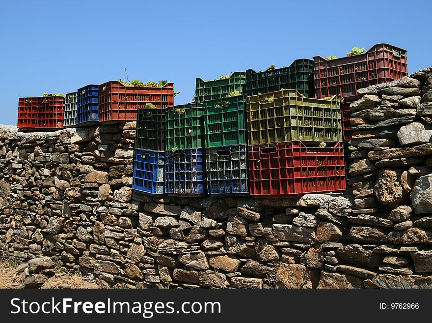 Colored crates of grapes on a stone wall.