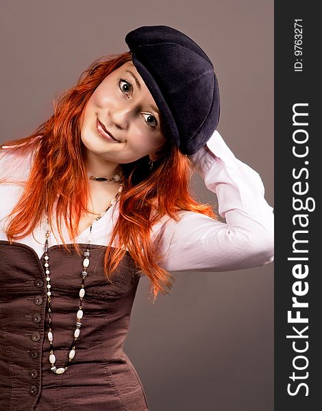 Red haired young woman in hat smiling isolated over grey